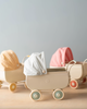 Toy prams, including a Maileg Micro Pram, in beige and pink, with a face mask placed in one, against a soft blue background, symbolizing childhood in the context of health safety.