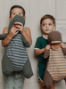 Two young children stand against a neutral background, each holding a Maileg Large Dark Green Gantosaurus Dinosaur. The child on the left holds a green striped Maileg Large Dark Green Gantosaurus Dinosaur close to their face, while the child on the right holds a brown striped dinosaur made from soft mix fabric, looking off to the side.