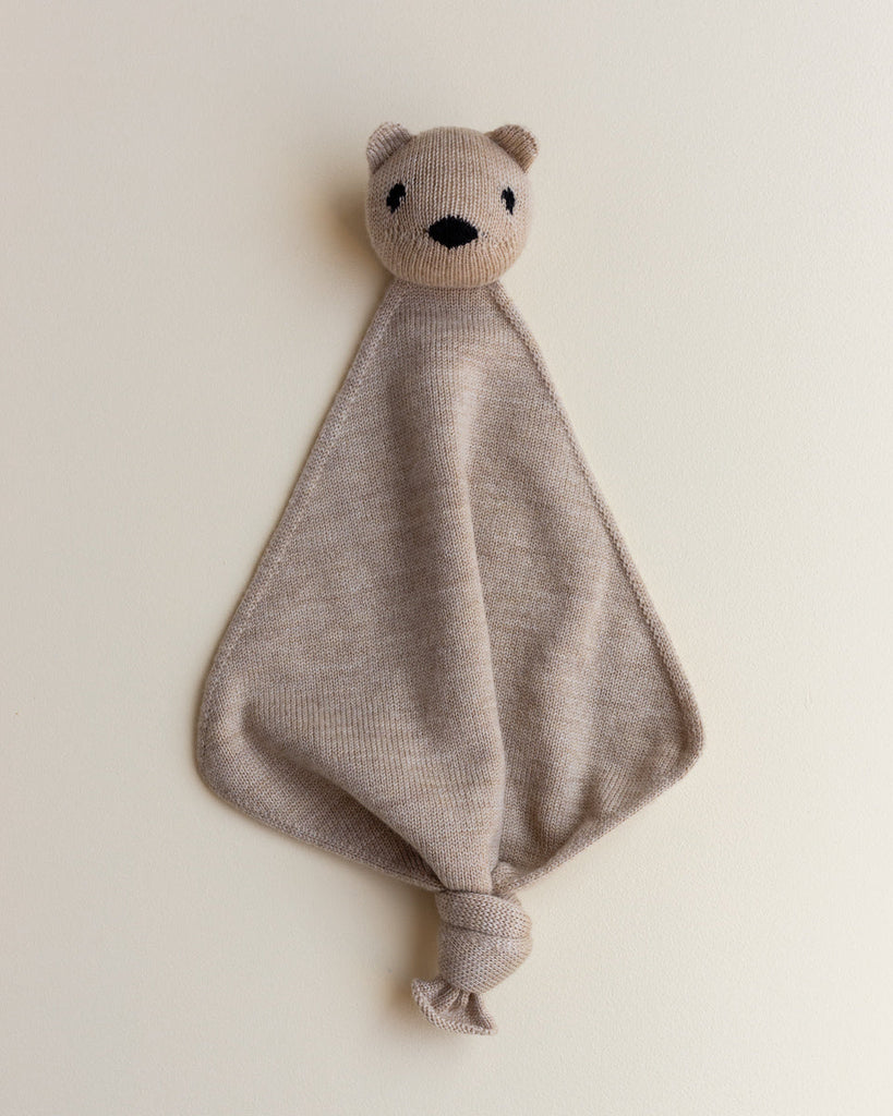 A beige small merino wool lovey with a head of a teddy bear at top.