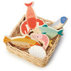 A collection of colorful wooden fish and a seashell toy pieces neatly arranged inside a small handcrafted Market Basket on a white background.