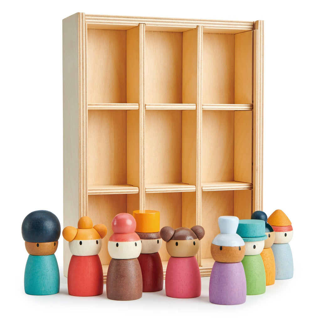 A solid wood display shelf with nine compartments stands in the background. In front of the shelf, the Happy Folk Hotel, with ten colorful peg dolls, each with unique hats and clothing, is arranged in a line for endless creative play. Painted in shades of red, green, blue, purple, orange, and yellow, they inspire open-ended play.