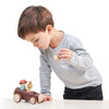 Young boy playing with a Timber Taxi vehicle and Merrywood folks on a table, focused intently on placing a figure into the driver's seat.