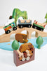 A colorful wooden Wild Pines Train Set featuring animals, trees, and various vehicles like a car, logging truck, and train on a play mat with roads and scenery.