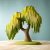 A Large Wooden Willow Tree, resembling a willow, with green leaf-like sections cascading down from thick branches, is placed on a light wooden surface against a teal background. The Large Wooden Willow Tree has a brown trunk and stands on a green base, painted with non-toxic paint.