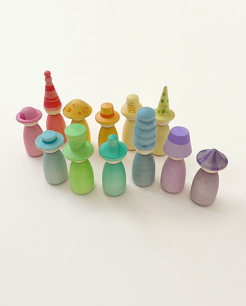 A group of colorful, wooden Grapat Fancy Nins with interchangeable hats arranged on a white background. Each doll is painted in a different pastel color, and the hats feature various patterns and shapes.