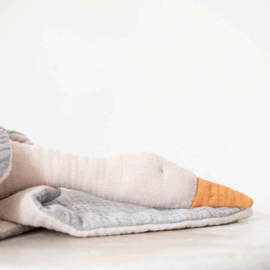 A Seagull Mobile with one foot prominently displayed, featuring a grey and white design with an orange toe, crafted from hypoallergenic plant fiber, resting on a soft, light-colored fabric surface