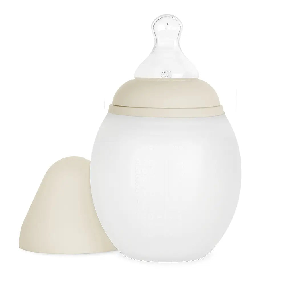 A beige and white Medical Grade Silicone Baby Bottle with a soft silicone body and a detachable nipple cover, designed to mimic breastfeeding, isolated on a white background.