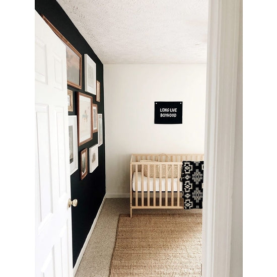 Long live boyhood banner in black color photographed against white wall inside a nursery room. 