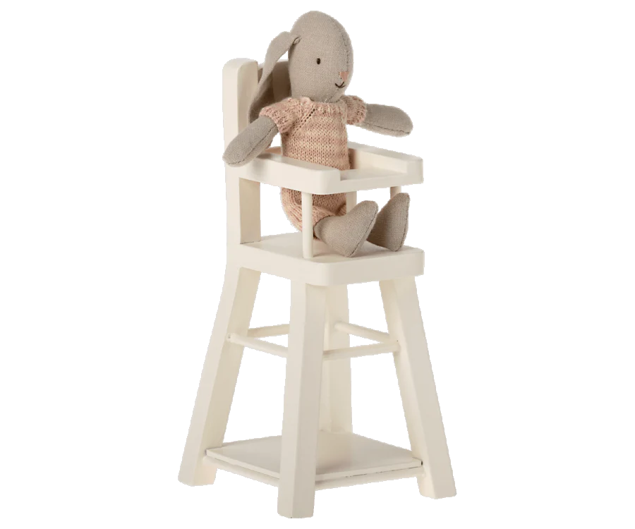 A stuffed gray rabbit in a pink knitted outfit sits in a Maileg Micro High Chair designed for micro-sized Maileg friends. The vintage-style high chair features a tray in front and a footrest below. With its ears pointed upward, the cheerful rabbit adds charm to any doll collection.