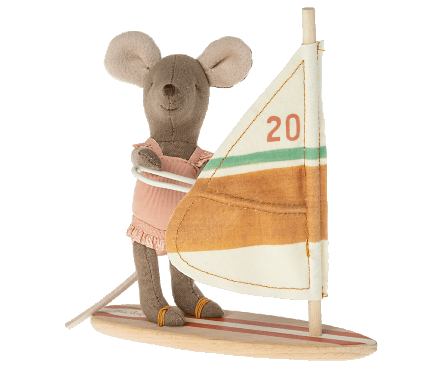 A Maileg Little Sister Surfer Mouse wearing a peach-colored outfit stands on a toy windsurf board, holding onto the white frame attached to a fabric sail. The sail, marked with the number "20," features horizontal green, orange, and yellow stripes. Elastic straps secure its magnetic hands to the frame for added stability.