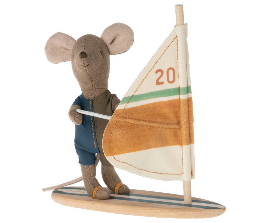 A Maileg Little Brother Surfer Mouse, dressed in a blue wetsuit, is holding onto the sail of a small windsurfing board using its magnetic hands. The sail is white with orange and green stripes, and the number 20 is printed on it. The mouse stands on a wooden base that resembles a surfboard.