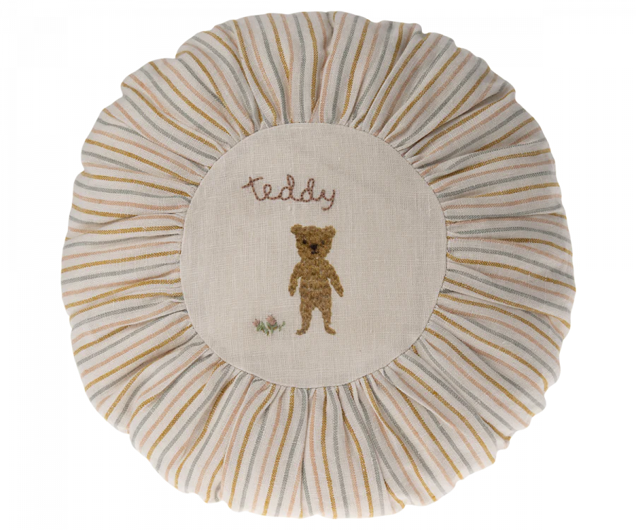 A round Maileg Cushion, Small with a central embroidered design featuring a teddy bear and the word "teddy", surrounded by striped beige and white pleated edging.