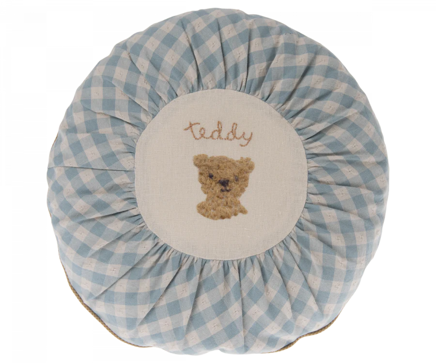 A round Maileg Cushion, Small with a blue and white checkered border, featuring an embroidered brown teddy bear and the word "teddy" in the center.