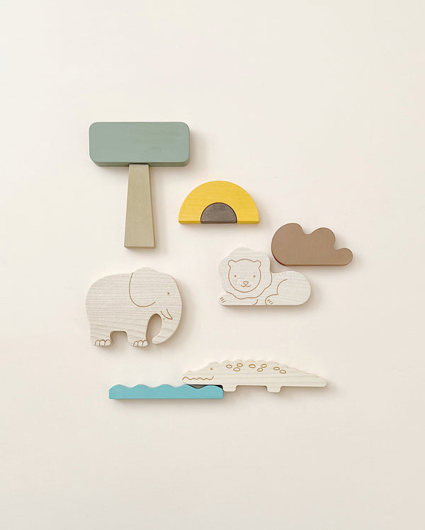 A flat lay of wooden toys, including hand-painted maple wood animals like a white elephant, a white lion, and a white crocodile with blue water underneath. The Wooden Safari Set offers more than just play—it’s perfect for fine motor skills development.